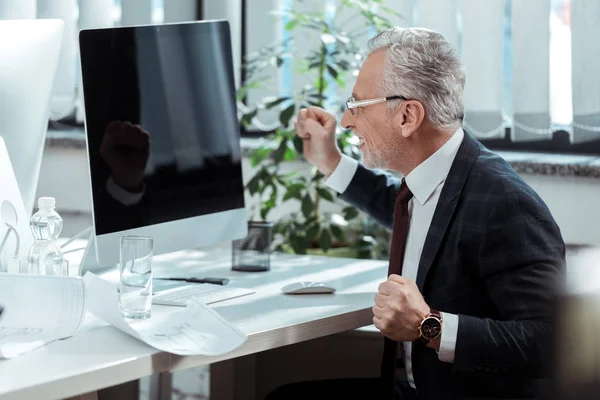 Счастливый бизнесмен в очках жестом рядом с монитором компьютера с пустым экраном — стоковое фото