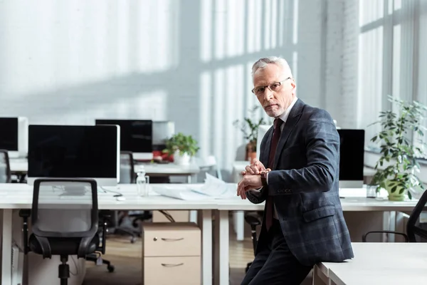 Bell'uomo d'affari in occhiali che tocca orologio in ufficio moderno — Foto stock