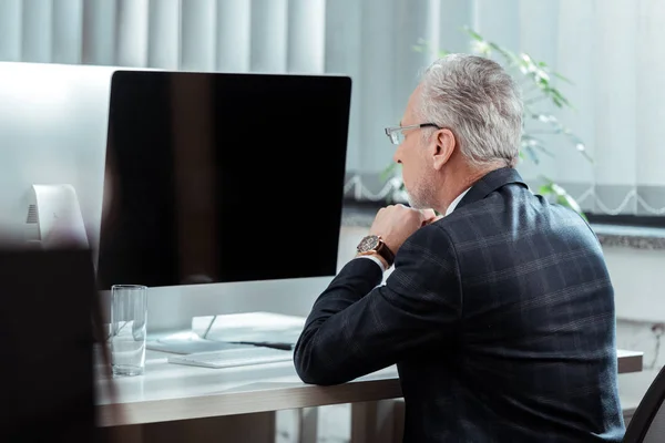 Enfoque selectivo de hombre de negocios guapo en gafas mirando el monitor de computadora con pantalla en blanco en la oficina - foto de stock