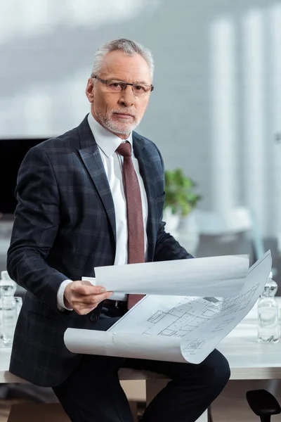 Handsome businessman in glasses holding blueprints in office — Stock Photo