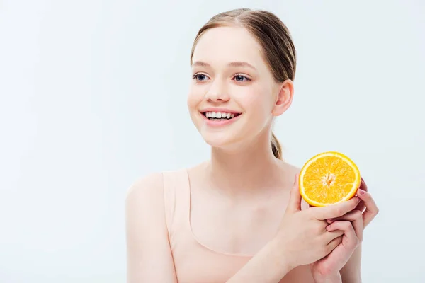 Feliz sonriente adolescente sosteniendo naranja mitad y mirando hacia otro lado aislado en gris - foto de stock