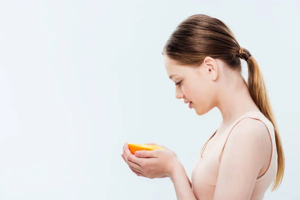 Vista lateral de adolescente sosteniendo naranja medio aislado en gris - foto de stock
