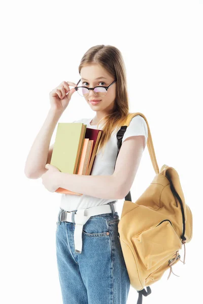 Smiling schoolgirl with backpack holding books and glasses isolated on white — Stock Photo