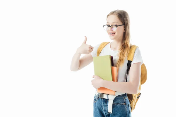 Усміхнена школярка з рюкзаком тримає книги і показує великий палець вгору ізольовано на білому — стокове фото