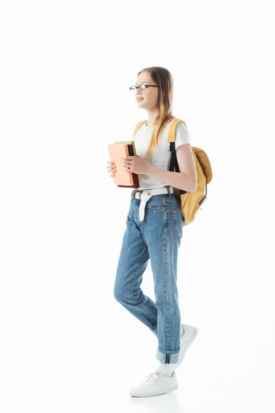 Écolière souriante avec sac à dos tenant des livres et marchant isolé sur blanc — Photo de stock