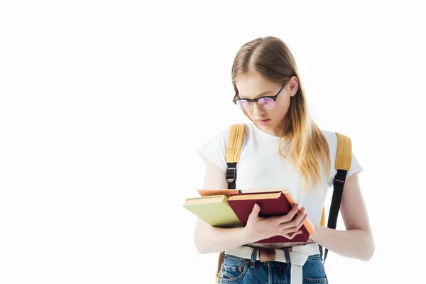 Schoolgirl in glasses with backpack reading book isolated on white — Stock Photo