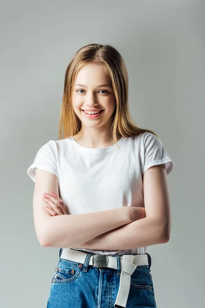 Heureuse adolescente avec les bras croisés regardant caméra isolé sur gris — Photo de stock