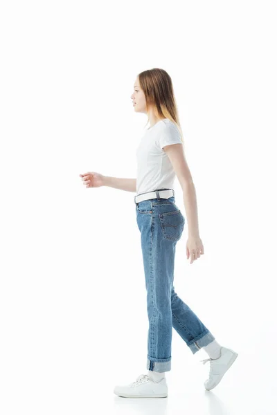 Vista lateral de la adolescente en pantalones vaqueros azules y camiseta blanca caminando aislado en blanco - foto de stock