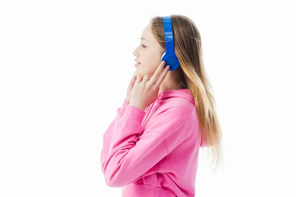 Vista lateral de una adolescente sonriente tocando auriculares azules en la cabeza aislada en blanco - foto de stock