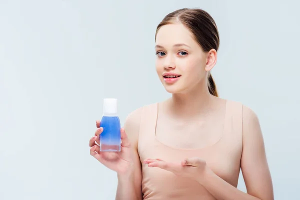 Pretty teenage girl presenting cosmetic lotion isolated on grey — Stock Photo
