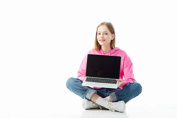 Smiling teenage girl with crossed legs holding laptop with blank screen isolated on white, illustrative editorial — Stock Photo