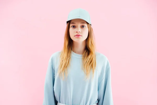 Triste bonita adolescente en gorra mirando cámara aislada en rosa - foto de stock