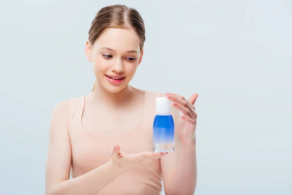 Smiling pretty teenage girl looking at cosmetic lotion isolated on grey — Stock Photo