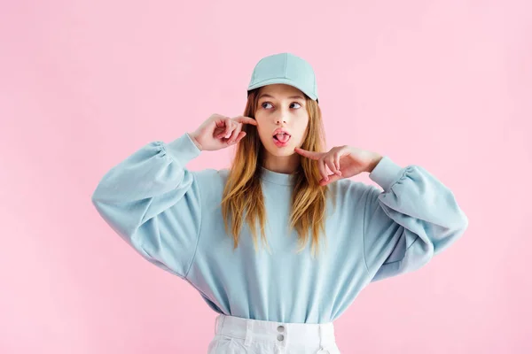 Pretty teenage girl in cap sticking out tongue isolated on pink — Stock Photo