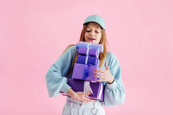 Feliz bonita adolescente en gorra celebración de cajas de regalo aislado en rosa - foto de stock