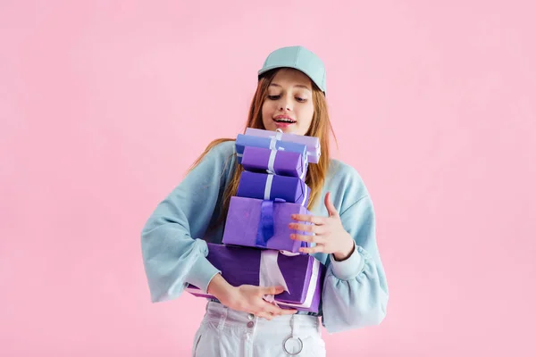 Happy pretty teenage girl in cap holding gift boxes isolated on pink — Stock Photo