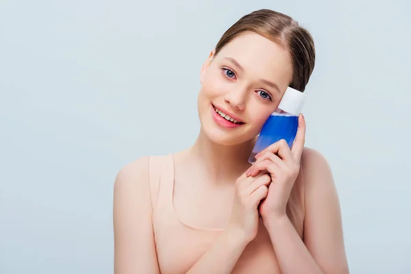 Menina bonita adolescente segurando loção cosmética azul isolado em cinza — Fotografia de Stock