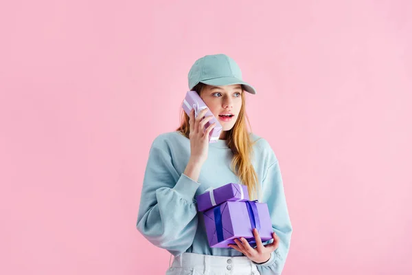 Surpris jolie adolescente en chapeau tenant présent comme téléphone isolé sur rose — Photo de stock