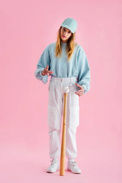 Full length view of pretty teenage girl in cap near baseball ball on bat on pink — Stock Photo