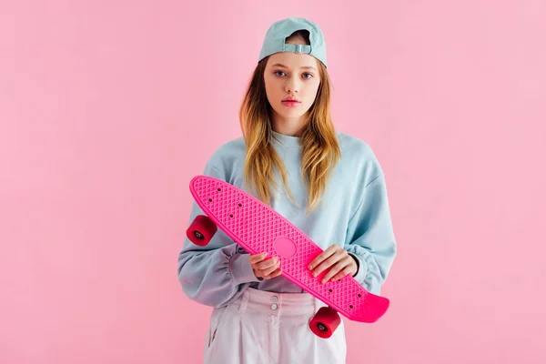 Pretty teenage girl in cap holding penny board isolated on pink — Stock Photo