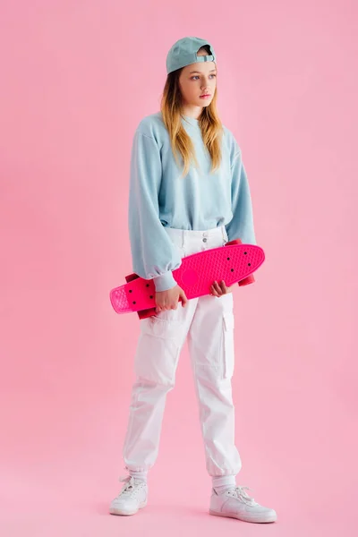 Hübsche Teenager-Mädchen mit Mütze hält Penny Board auf rosa — Stockfoto