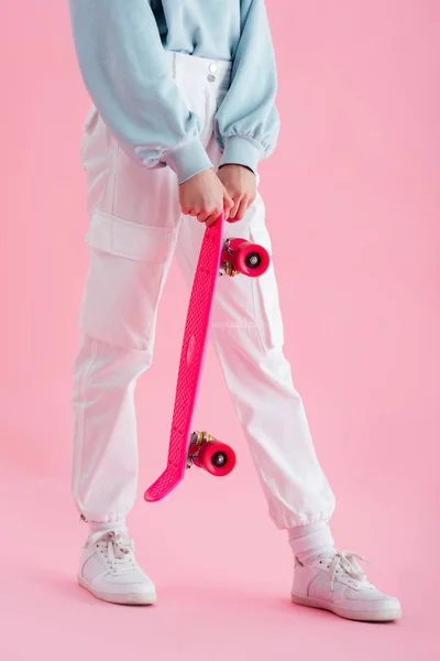 Recortado vista de adolescente chica sosteniendo penny board en rosa - foto de stock