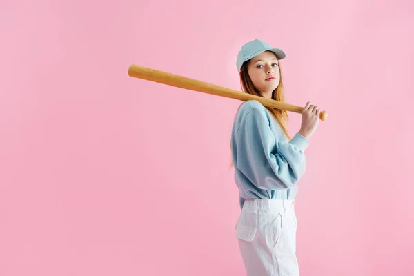 Красива дівчина-підліток у кепці тримає дерев'яну бейсбольну кажана ізольовано на рожевому — стокове фото