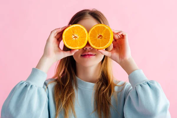 Pretty teenage girl holding orange halves in front of eyes isolated on pink — Stock Photo