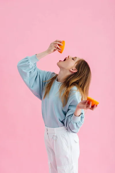Bella ragazza adolescente spremitura succo d'arancia in bocca isolato su rosa — Foto stock