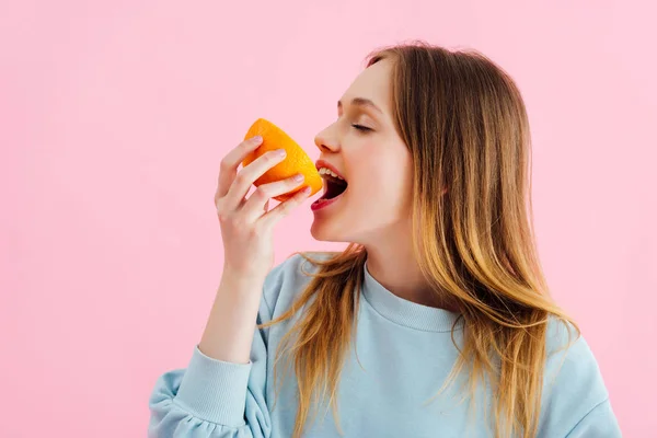 Hübsche Teenager-Mädchen mit geschlossenen Augen beißen orange halb isoliert auf rosa — Stockfoto