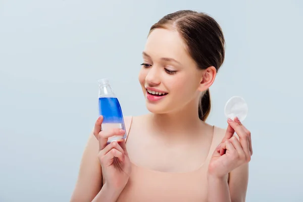 Pretty teenage girl holding blue lotion and cotton pad isolated on grey — Stock Photo