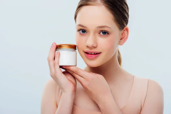 Smiling teenage girl holding container with cosmetic cream isolated on grey — Stock Photo