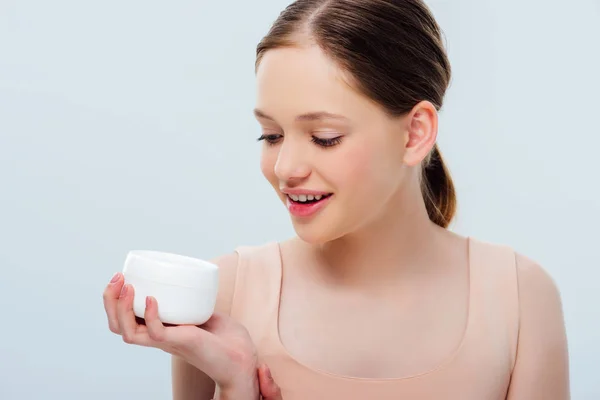 Cheerful teenage girl looking at cosmetic cream isolated on grey — Stock Photo
