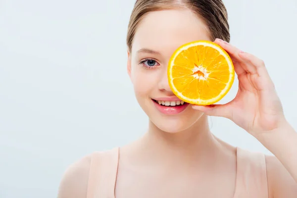 Adolescent fille avec sourire tenant orange mûr moitié près du visage isolé sur gris — Photo de stock