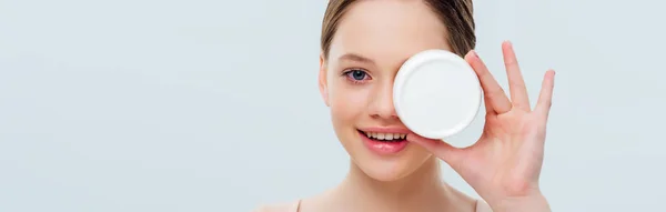 Cheerful teenage girl holding cosmetic cream isolated on grey, panoramic shot — Stock Photo