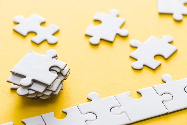 Selective focus of connected jigsaw near stack of puzzle pieces on yellow — Stock Photo