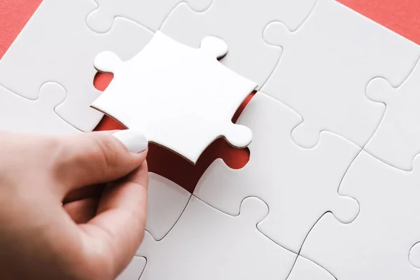 Cropped view of woman holding white jigsaw puzzle piece on red — Stock Photo