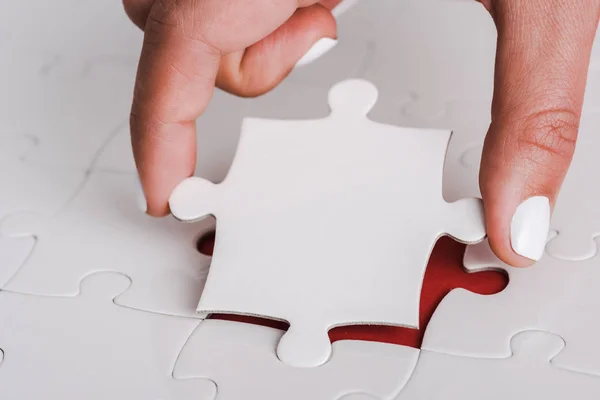 Close up of woman holding white jigsaw near connected puzzle pieces — Stock Photo