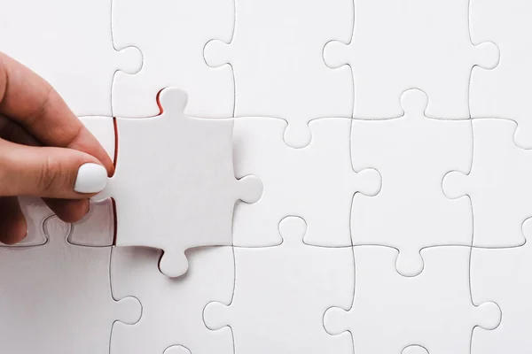 Top view of woman holding white jigsaw near connected puzzle pieces — Stock Photo