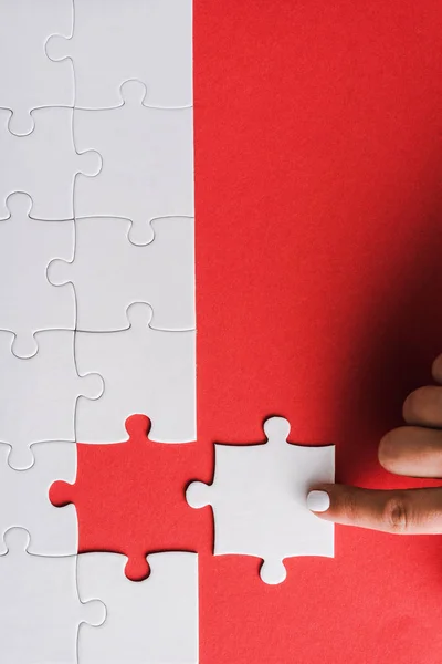 Top view of woman pointing with finger at white jigsaw near connected puzzle pieces on red — Stock Photo
