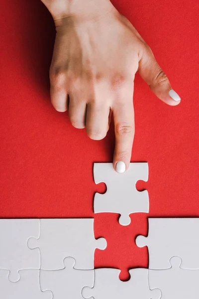 Draufsicht der Frau, die mit dem Finger auf Puzzleteile in der Nähe von miteinander verbundenen weißen Puzzleteilen auf Rot zeigt — Stockfoto