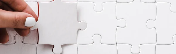 Panoramic shot of woman holding white jigsaw near connected puzzle pieces — Stock Photo