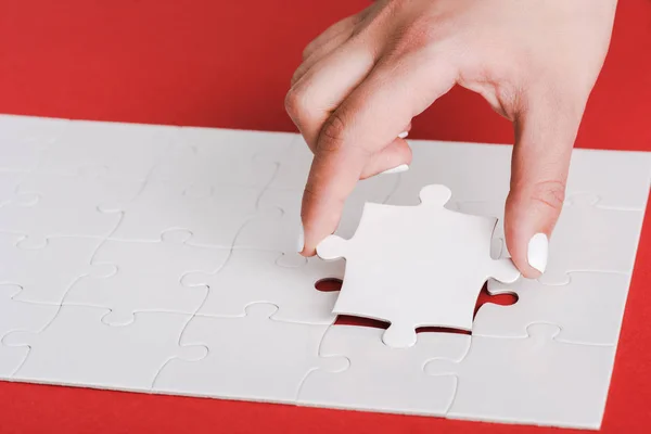 Abgeschnitten von Frau, die Puzzleteile in der Nähe zusammenhängender weißer Puzzleteile auf rot hält — Stockfoto