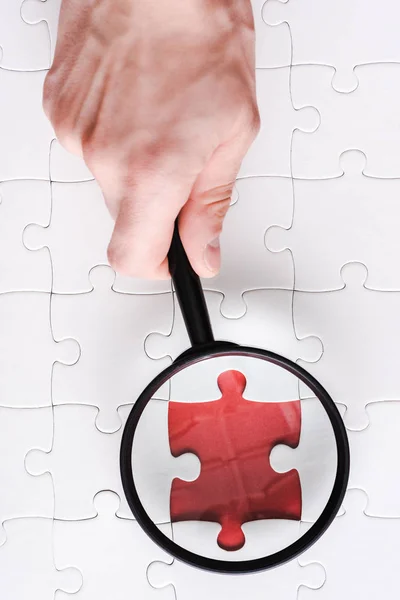 Top view of man holding magnifying glass near red jigsaw near white connected puzzle pieces — Stock Photo