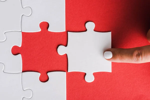 Vista ritagliata della donna che punta con il dito al puzzle vicino collegato pezzi di puzzle bianchi sul rosso — Foto stock