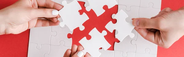 Panoramic shot of man and woman holding white puzzle pieces on white — Stock Photo