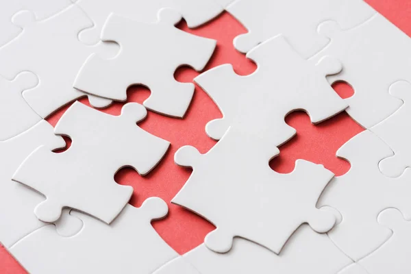 Unfinished jigsaw near connected white puzzle pieces on red — Stock Photo