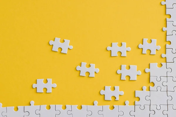 Top view of unfinished jigsaw near connected white puzzle pieces isolated on yellow — Stock Photo