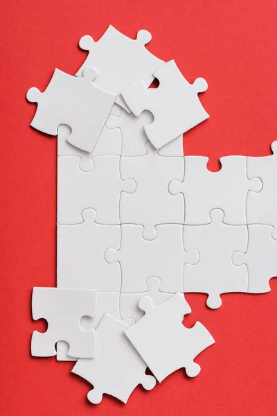 Vue de dessus du puzzle blanc inachevé près de pièces de puzzle reliées isolées sur rouge — Photo de stock