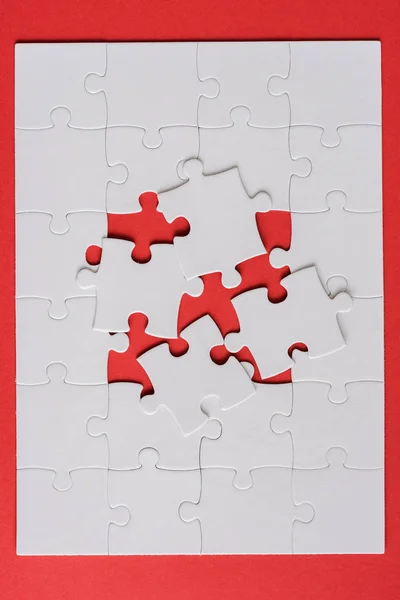 Верхний вид белой головоломки рядом с соединенными кусочками головоломки на красном — стоковое фото